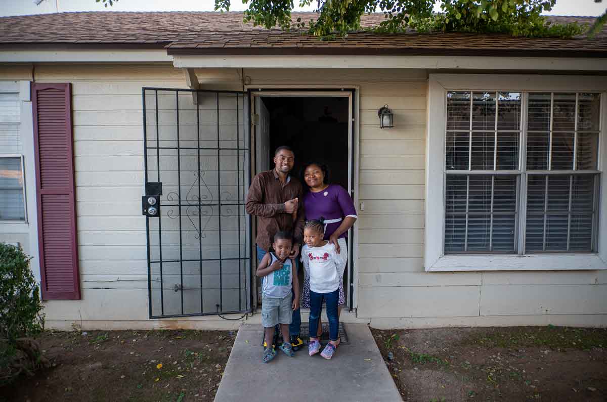 A refugee family learning standing in front of their house.