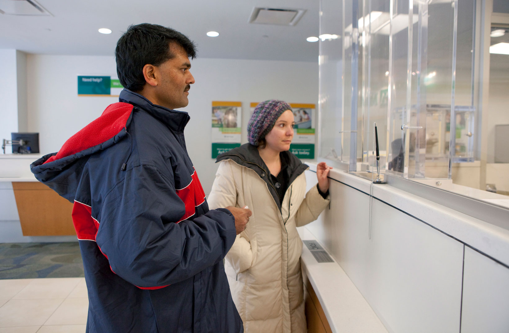 A refugee and resettlement staff member standing in front of a bank teller. IRC/MCohen