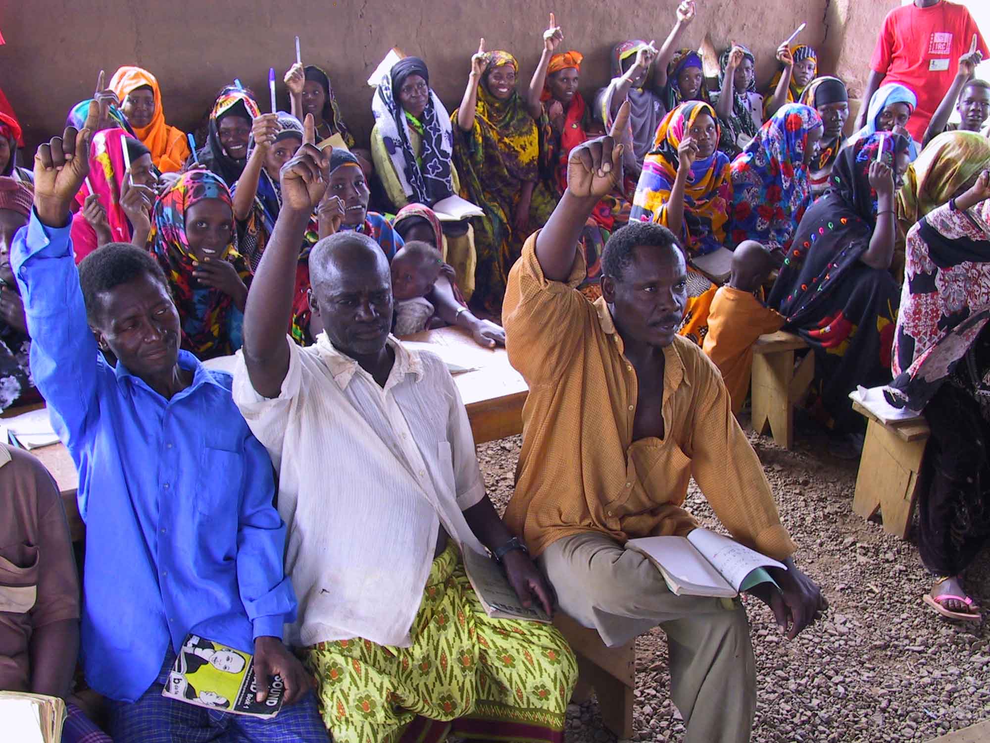 A photograph of student refugees raising their hands during class. IRC